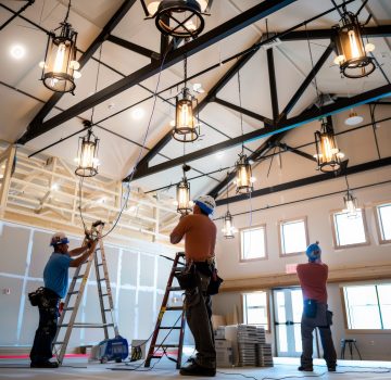 Team of skilled electricians working on installing lighting fixtures inside a modern commercial building with high ceilings. Team of skilled electricians working on installing lighting fixtures inside a modern commercial building with high ceilings.